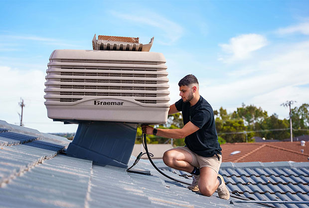 A technician installs or maintains a rooftop evaporative cooler.